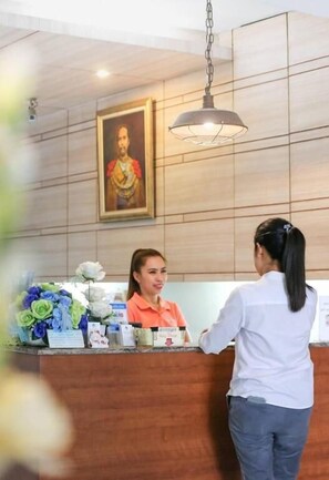 Un mostrador de recepción con un retrato enmarcado encima, un colgador de luz y un arreglo floral en la barra.