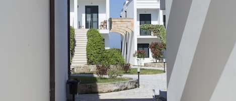 Un pasillo con un arco de piedra que da a un edificio blanco con balcón y paneles solares.
