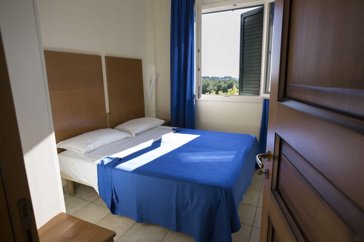 Ein Schlafzimmer mit einem Bett, einem Fenster mit Vorhängen und einer Holztür.
