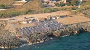 An aerial view of a coastal area with a pier extending into the water, surrounded by rocky terrain and sparse vegetation. - Hotel Residence Portoselvaggio (Nardò)