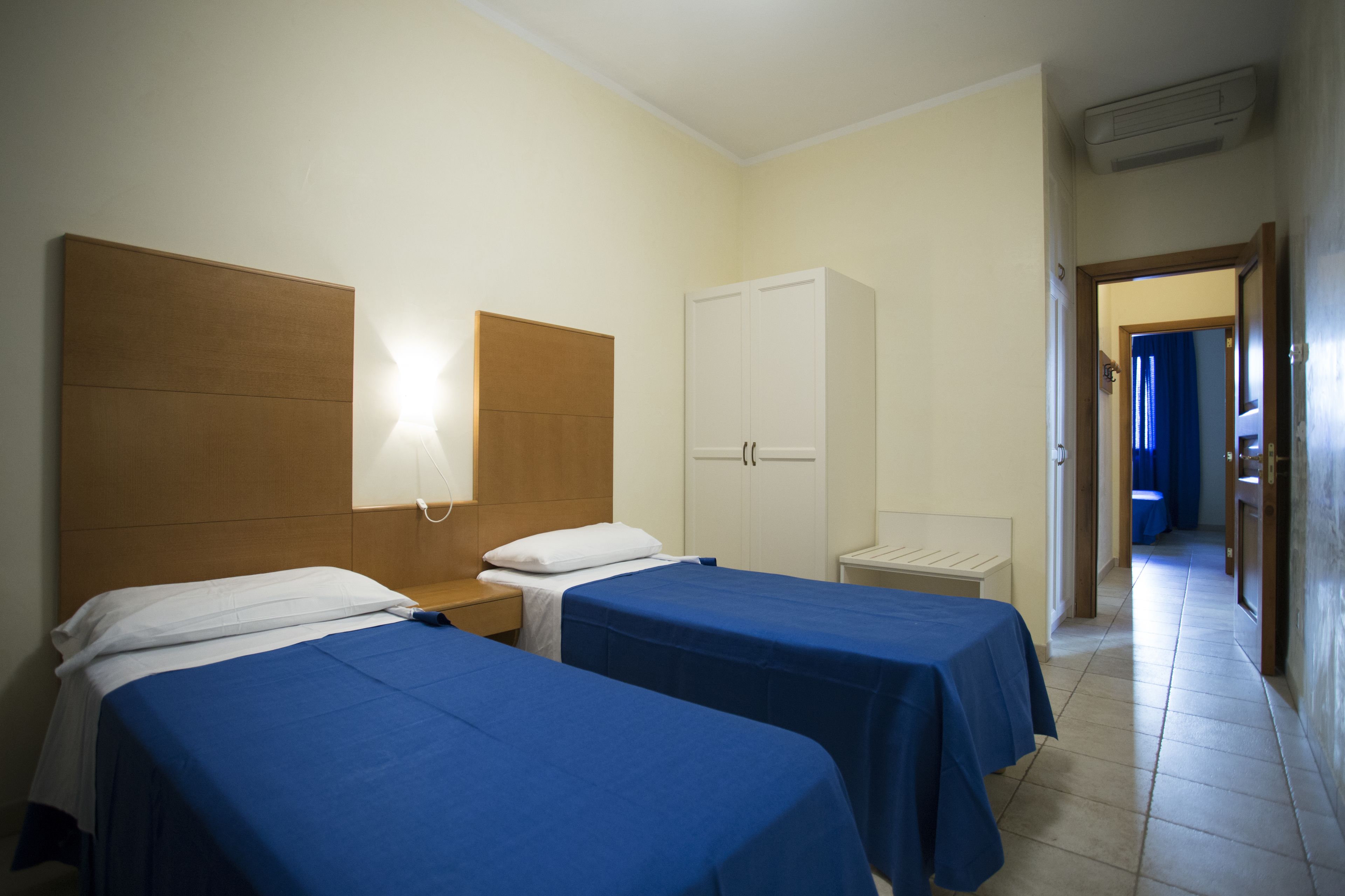 Habitación de hotel con dos camas individuales, un armario, una mesita de noche y un baño visible a través de una puerta abierta.