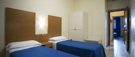 Habitación de hotel con dos camas individuales, un armario, una mesita de noche y un baño visible a través de una puerta abierta.
