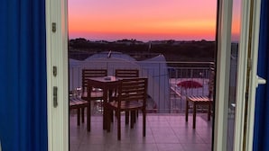 A balcony with a table and chairs, a view of the sunset, and a tent in the background. - Hotel Residence Portoselvaggio (Nardò)