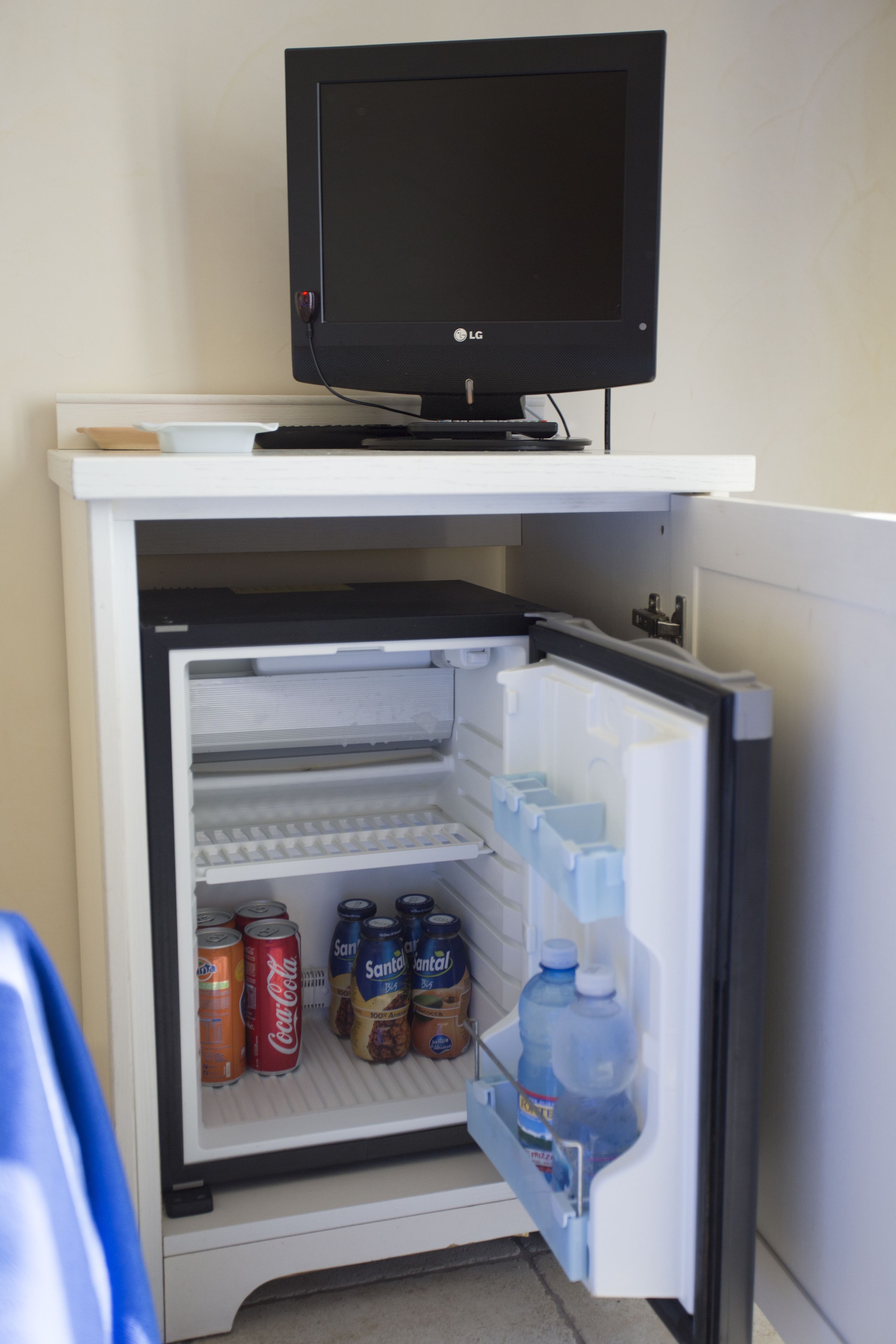 A small refrigerator with a television on top, containing beverages and cans.
