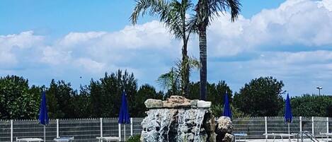 Una piscina azul clara con una palmera y una formación rocosa en el centro.