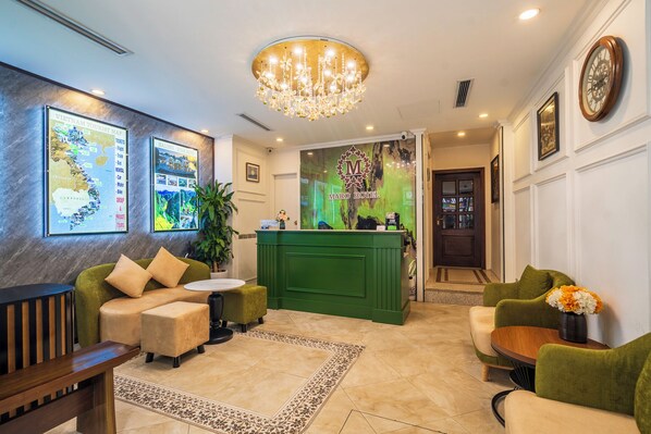 A hotel lobby with a reception desk, seating area, and a chandelier.