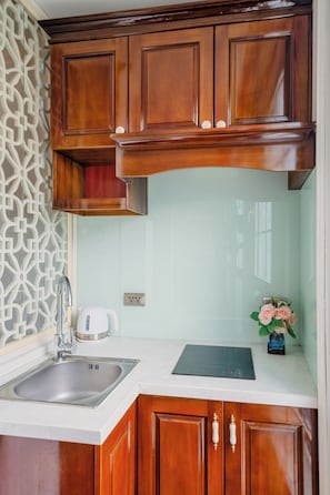 A kitchen with wooden cabinets, a stainless steel sink, a white kettle, and a vase with flowers. - Hanoi Maro Hotel (Hanoi)