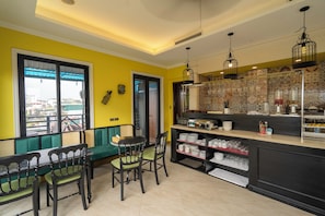A dining area with a green sofa, two chairs, a table, and a kitchen counter with various items. - Hanoi Maro Hotel (Hanoi)
