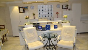 A modern kitchen with two white cushioned chairs, a glass-top table, and a display of clocks and flowers on the wall.