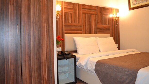 A hotel room with a wooden headboard, a bed with white linens, a nightstand with a phone and a vase of flowers, and wall-mounted lamps.