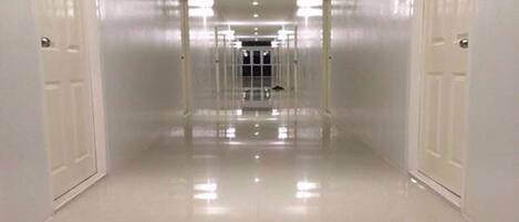 Un pasillo largo y estrecho con paredes y puertas blancas a ambos lados, que conduce a un par de puertas dobles al final.