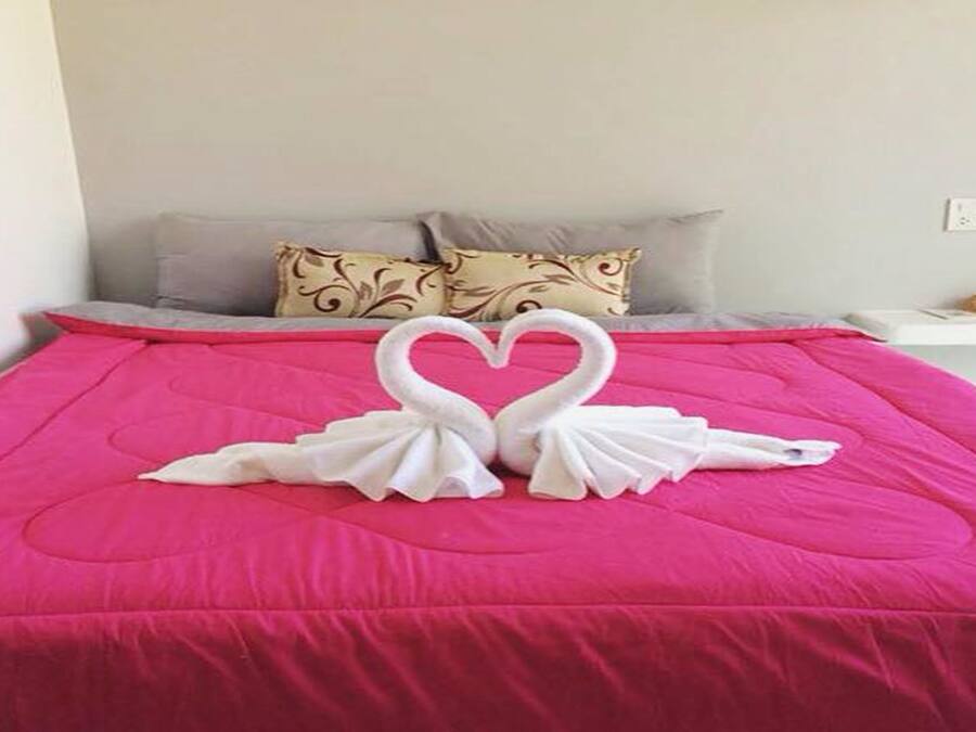 A bed with a pink bedspread and two white towels arranged in the shape of swans.