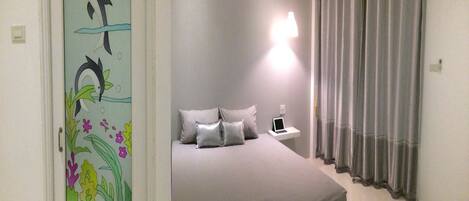 Un dormitorio con cama, mesita de noche, ordenador portátil y cortina.