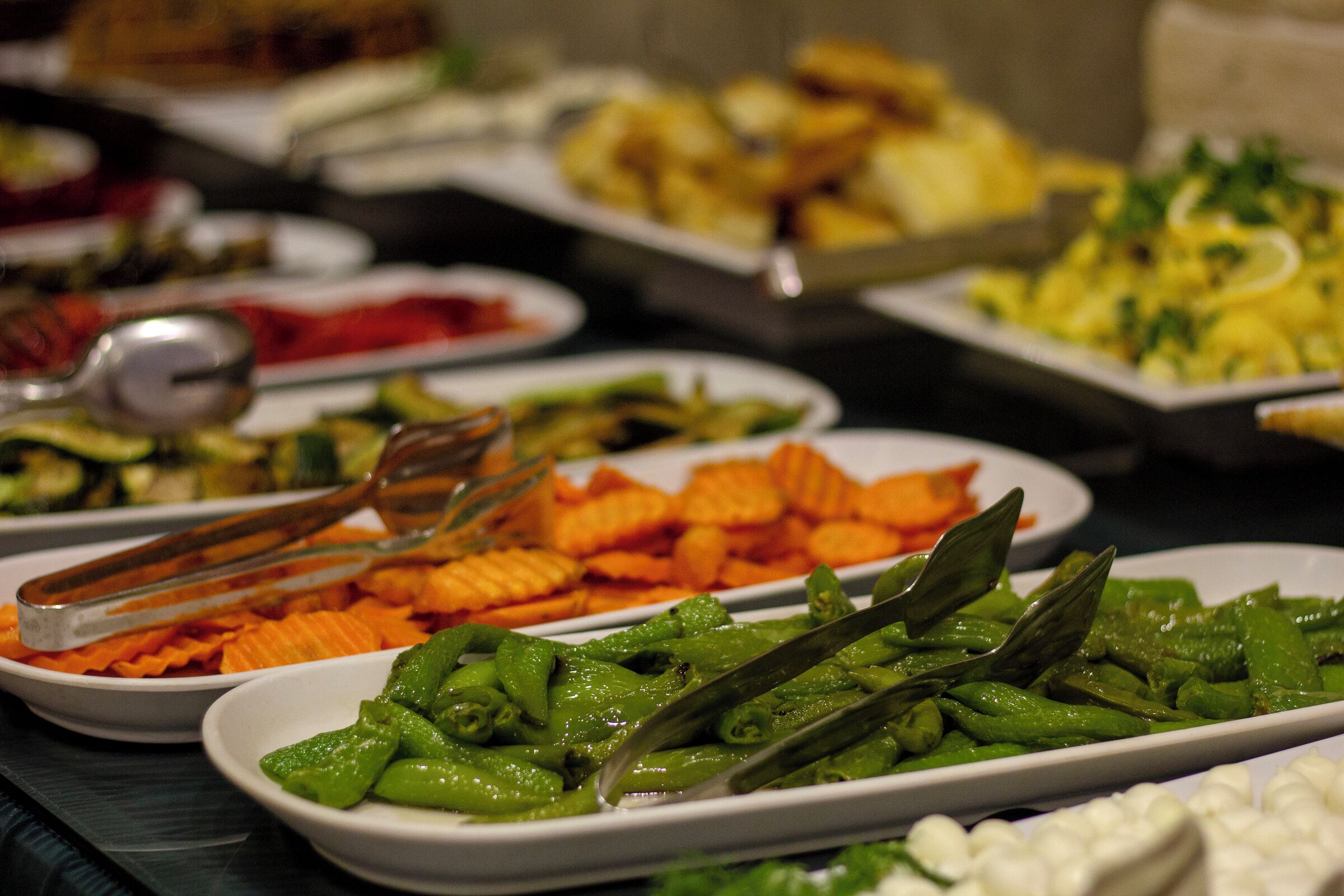 A buffet with various dishes including green beans, carrots, and other vegetables.