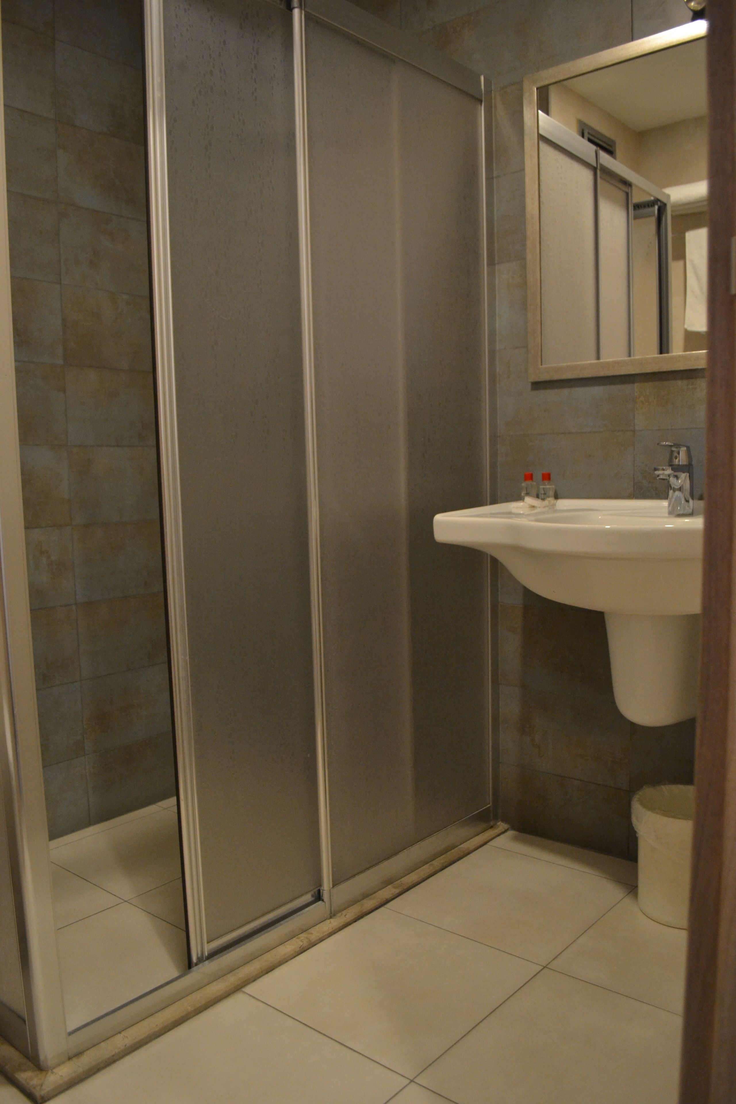 A bathroom with a glass shower enclosure, a sink, and a mirror.