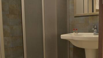 A bathroom with a glass shower enclosure, a sink, and a mirror.