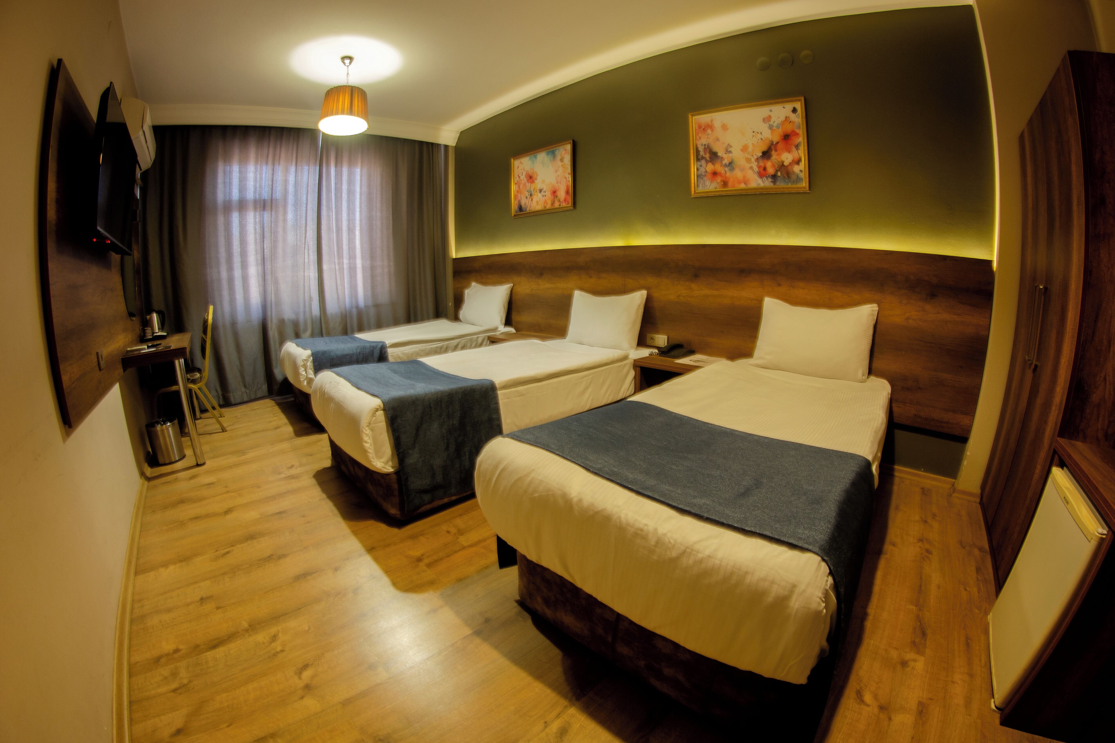 A hotel room with two beds, wooden flooring, a flat-screen TV, a desk, and a large window with curtains.