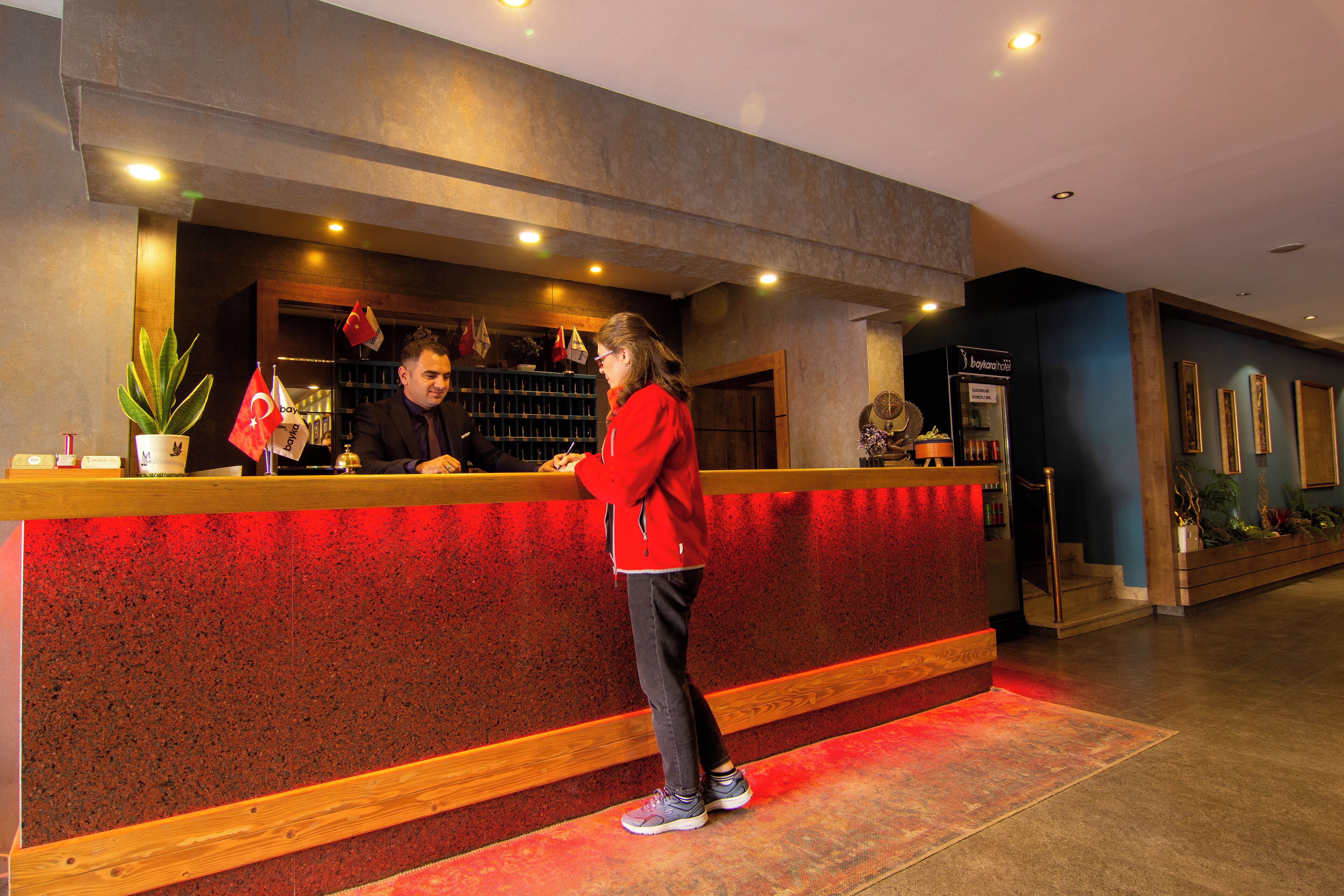 A reception desk with a red counter, a potted plant, and flags.