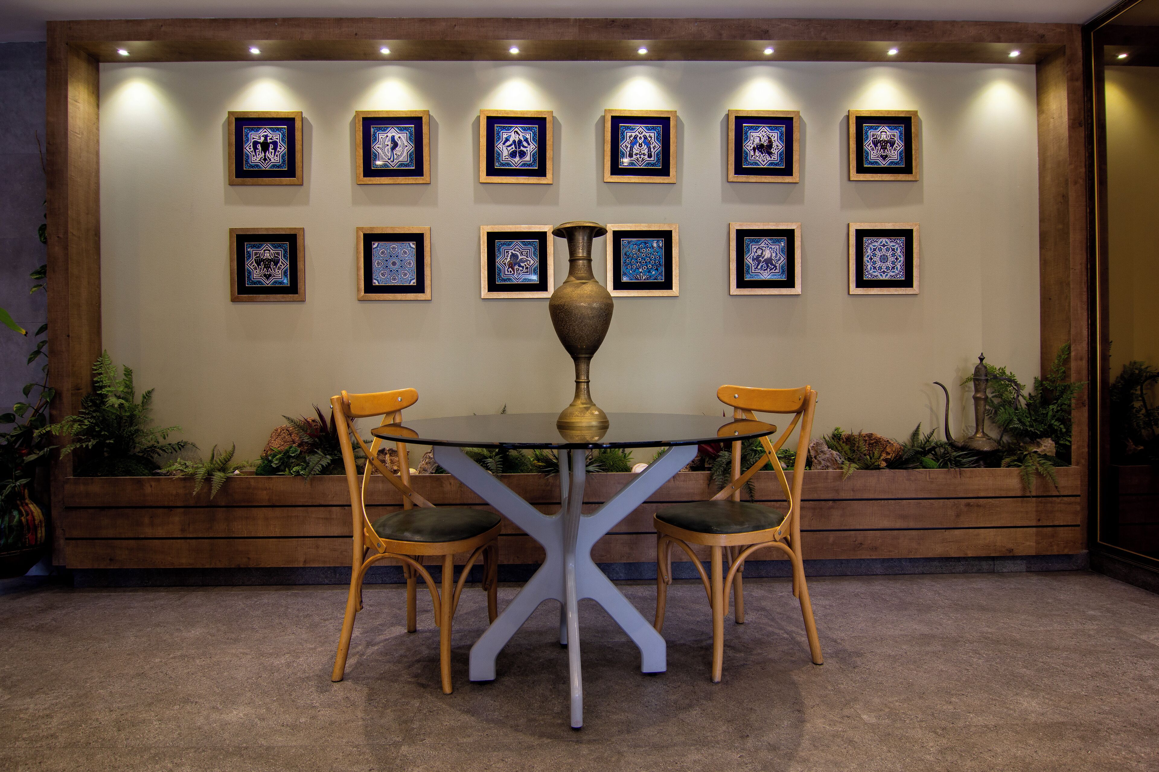 A dining area with a round table and four chairs, framed artwork on the wall, and wooden planters with plants.