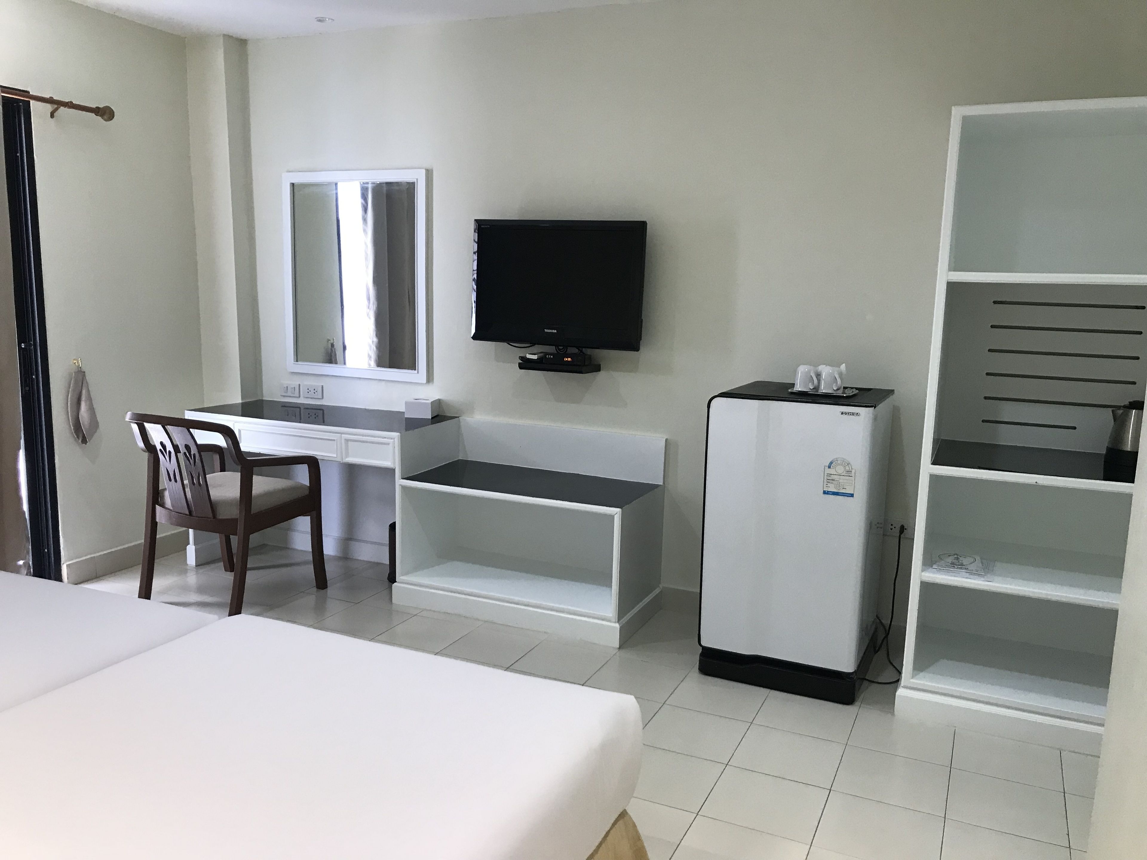 A hotel room with a bed, a desk, a chair, a television, and a mini-fridge.