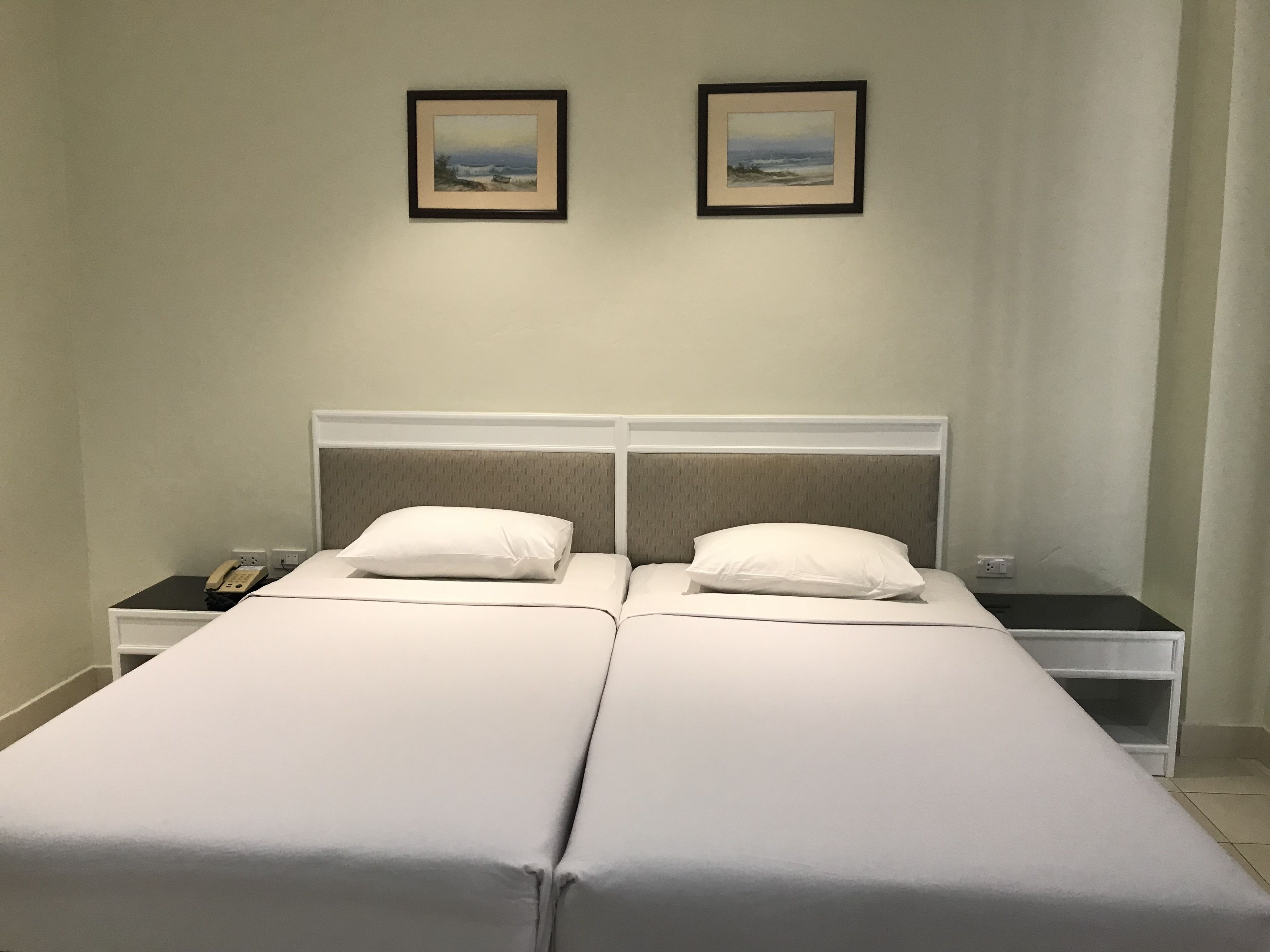 A double bed with white bedding, two bedside tables with lamps, and two framed pictures on the wall.