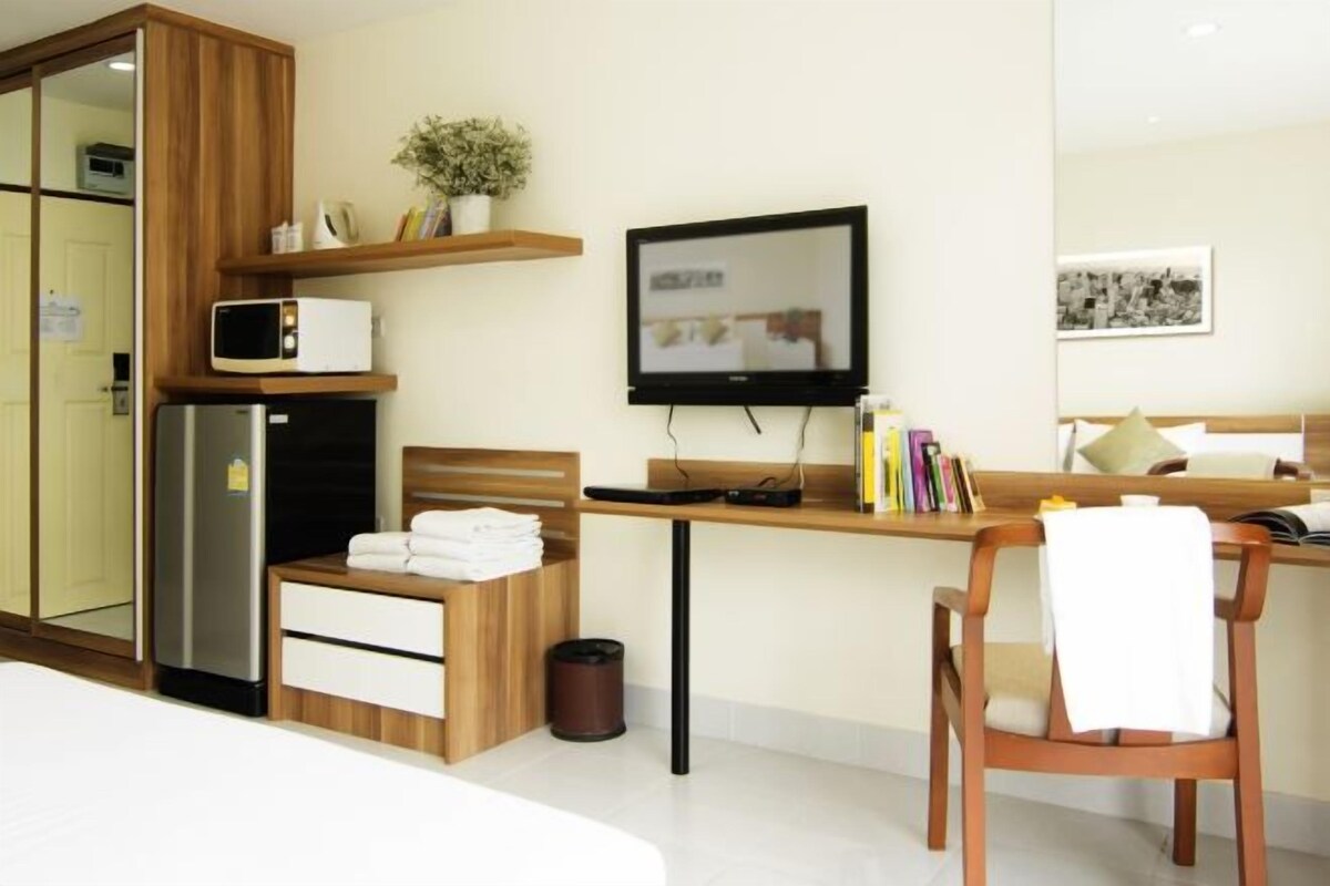 Una habitación de hotel moderna con un escritorio de madera, un televisor de pantalla plana, un microondas, un refrigerador, una silla y una cama.
