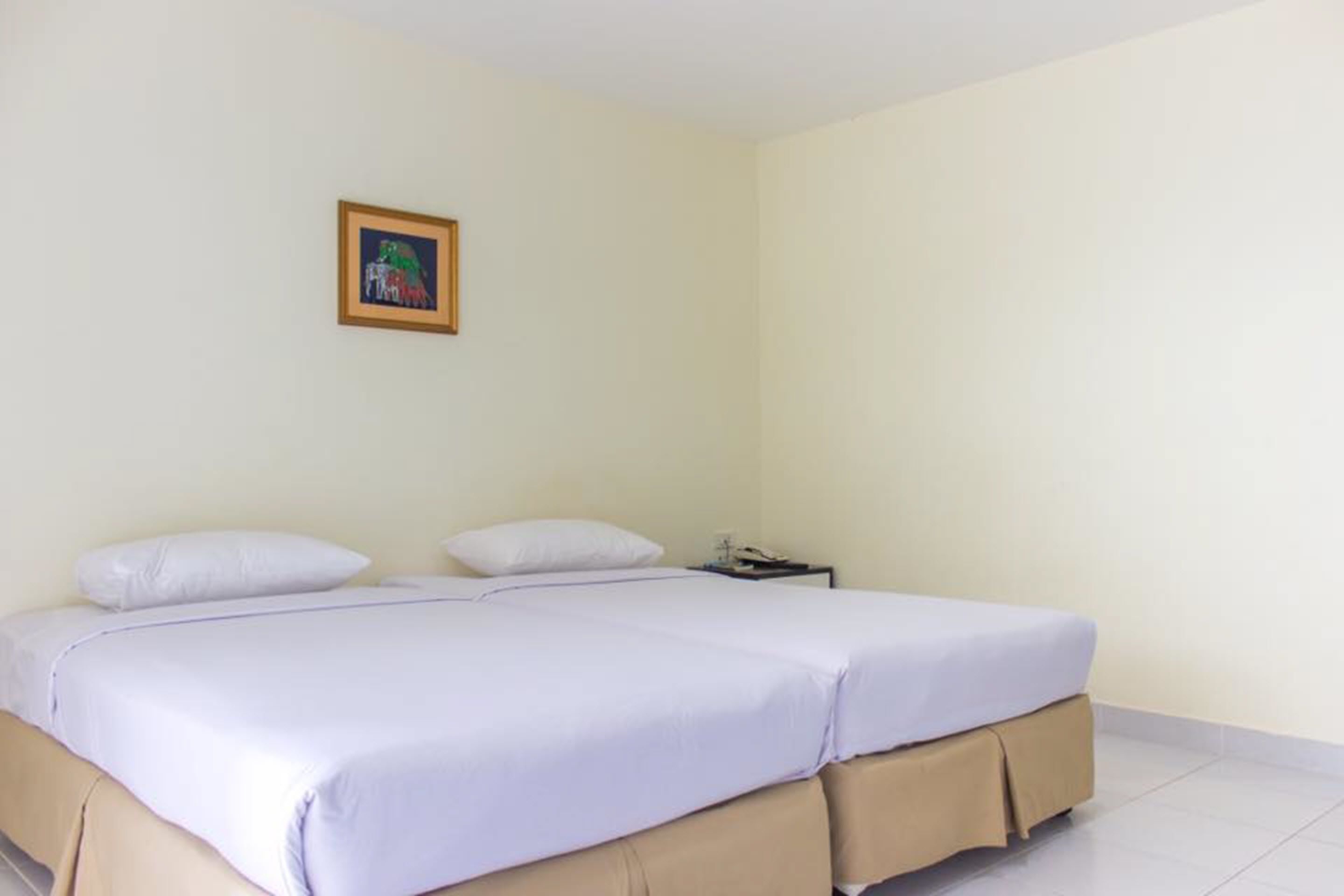Una camera singola con una coperta beige, un piccolo comodino e un quadro appeso al muro.