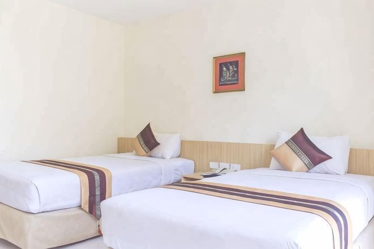 A hotel room with two beds, each with a pillow and a blanket.