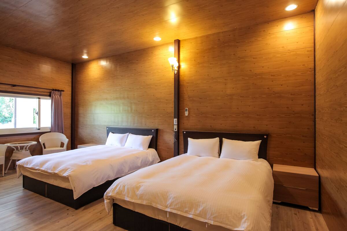 A room with two beds, wooden walls, and a small table with chairs.
