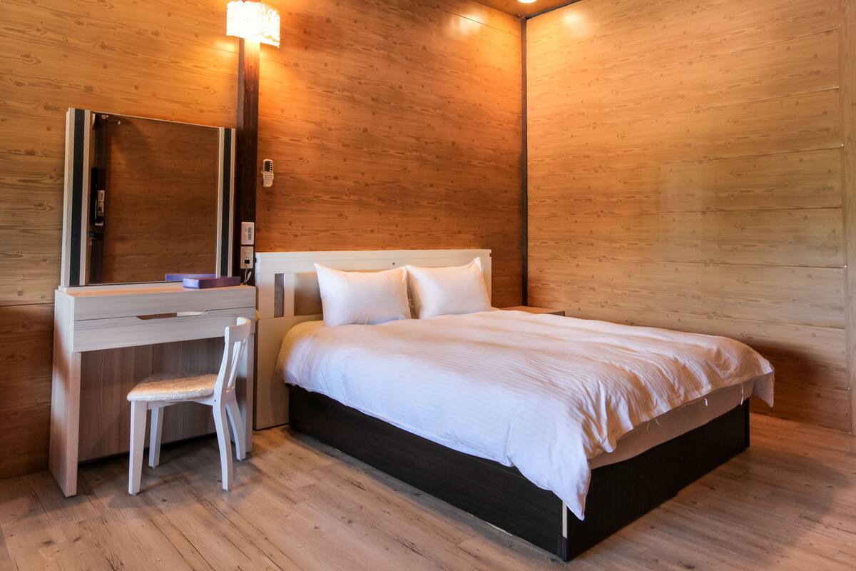 A wooden-paneled room with a bed, a desk, and a chair.