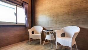 Ein Zimmer mit Holzwänden, einem fenster mit Vorhängen und zwei Korbstühlen um einen kleinen runden Tisch.