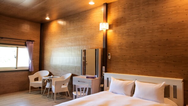 Ein Hotelzimmer mit Holzvertäfelung, einem Bett mit weißer Bettwäsche, einem Schreibtisch mit Stuhl und einem Fenster mit Vorhängen.