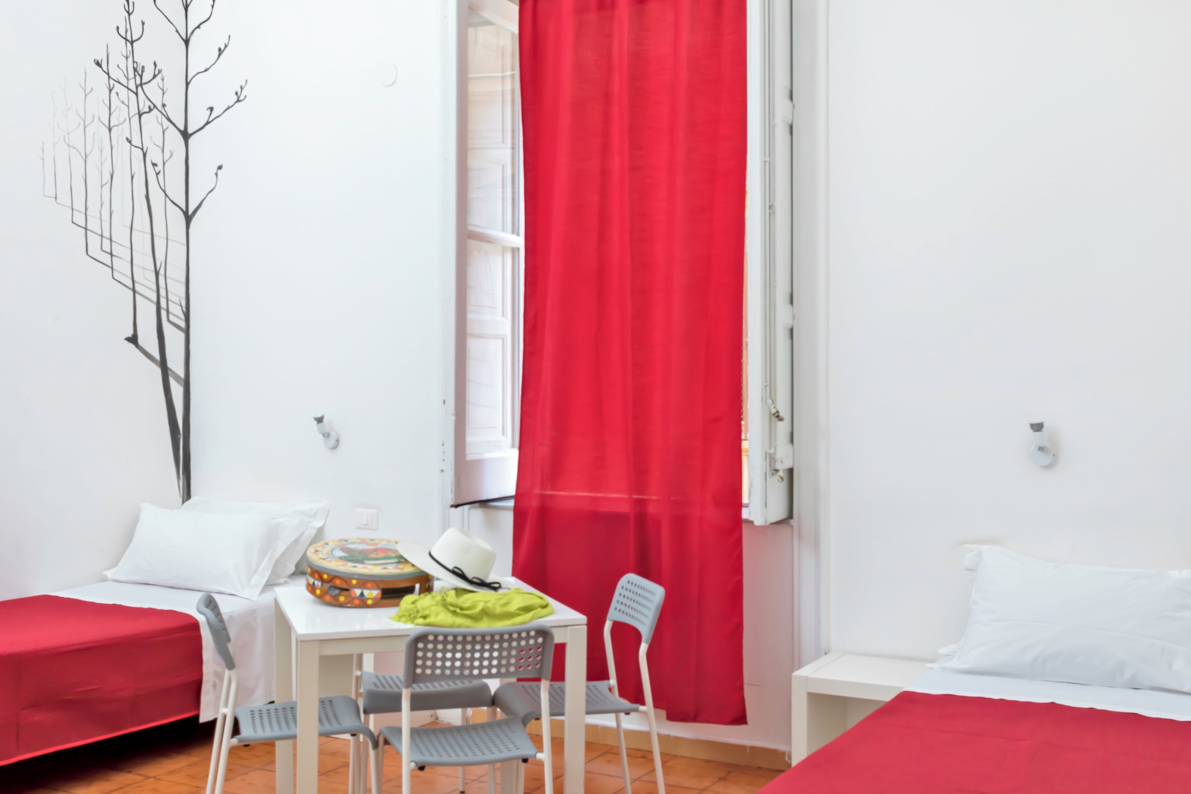 A room with a bed, a table with chairs, a red curtain, and a wall art piece.