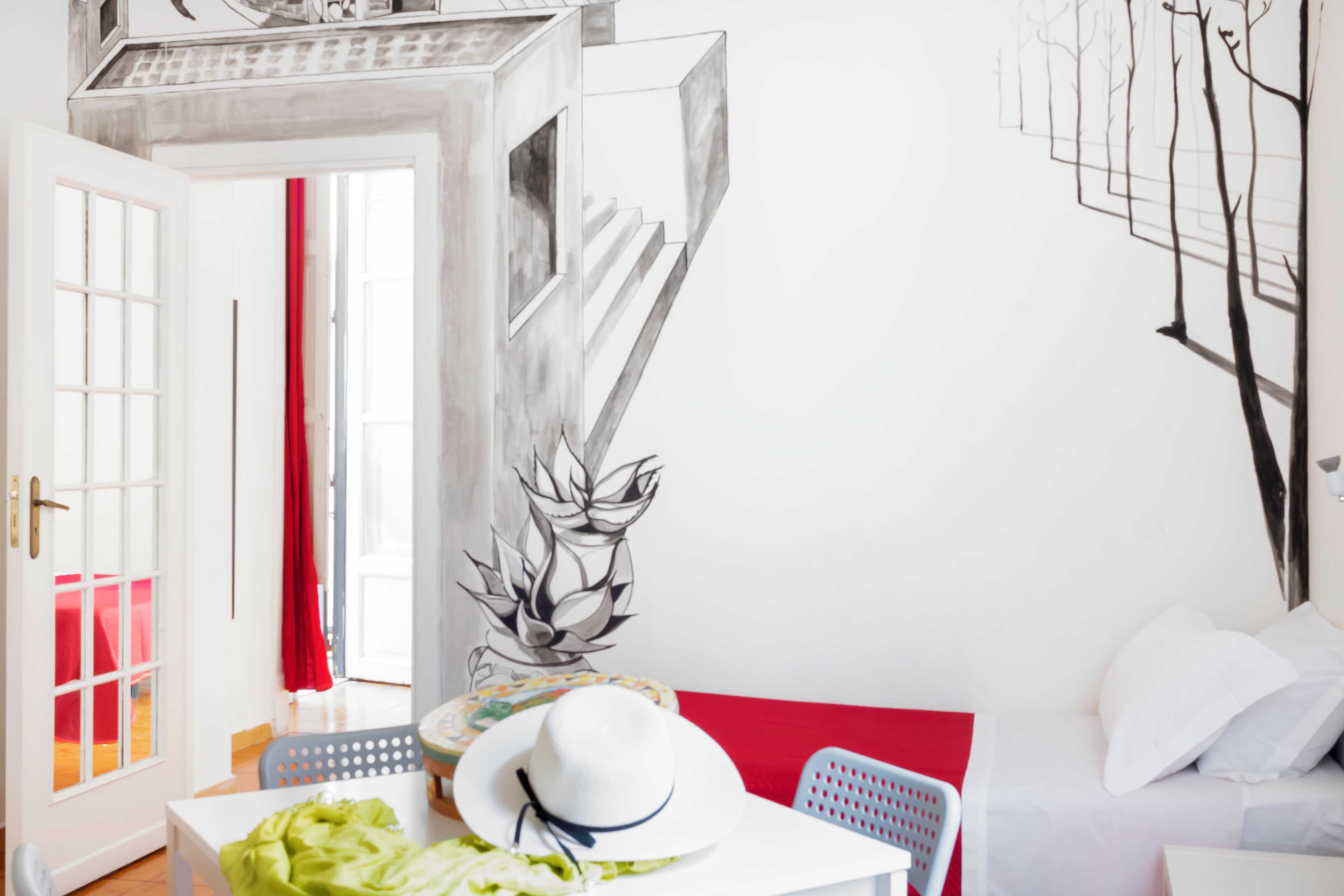 Ein modernes Zimmer mit weißer Wand, einem roten Vorhang, einem weißen Hut auf einem Tisch und einem schwarz-weißen Baum-Wandbild.
