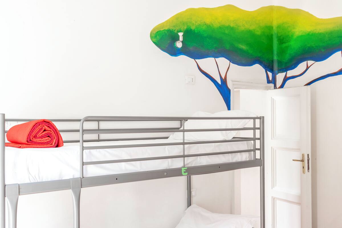 Ein Stockbett mit einem roten Handtuch, einer weißen Tür und einem Wandgemälde mit Bäumen.