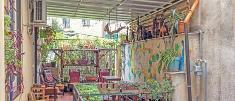 A covered outdoor area with potted plants, wooden furniture, and a metal railing.