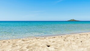 Una playa arenosa con agua turquesa cristalina y una pequeña colina al fondo.