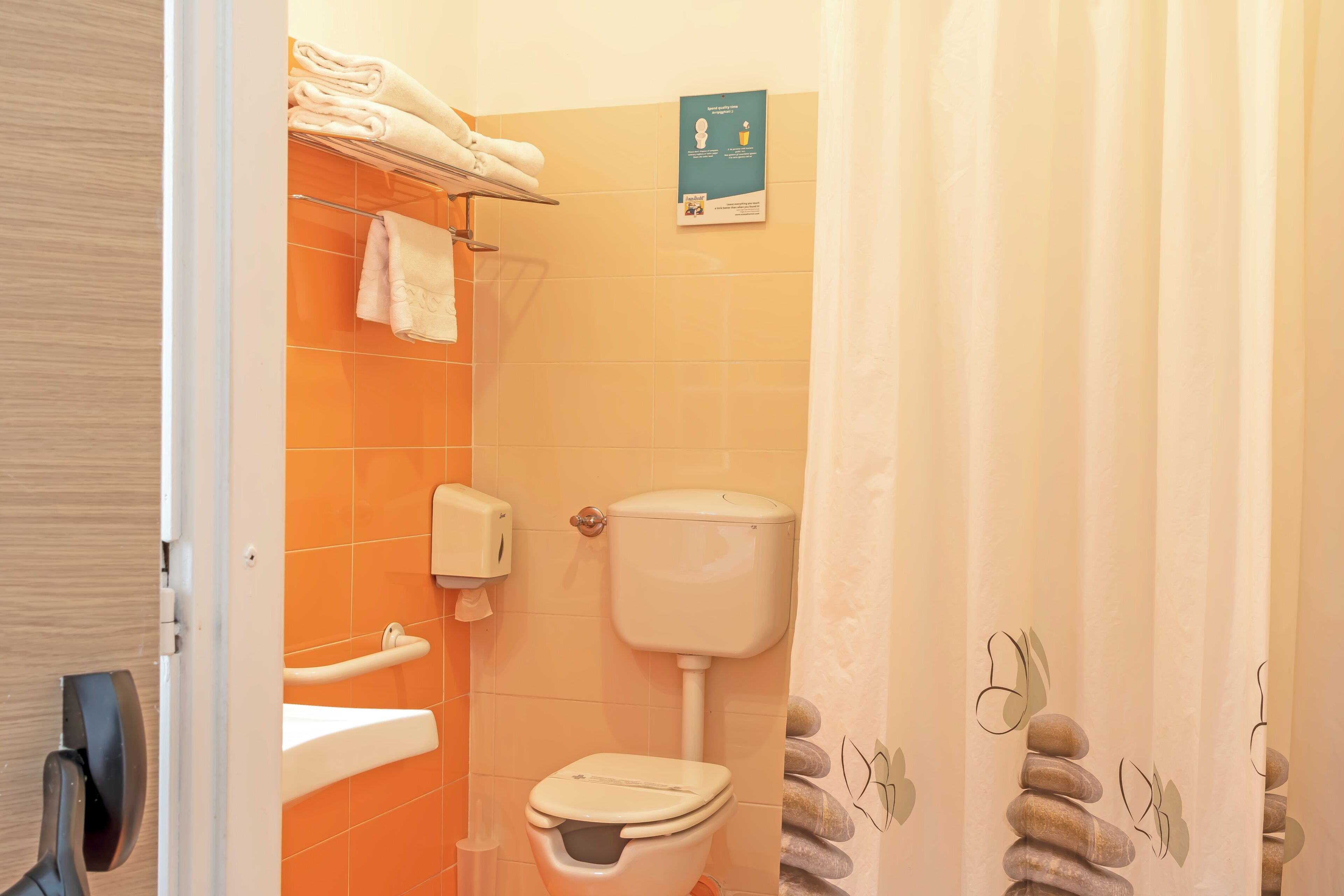 A bathroom with an orange tiled wall, a toilet, a sink, and a towel rack.
