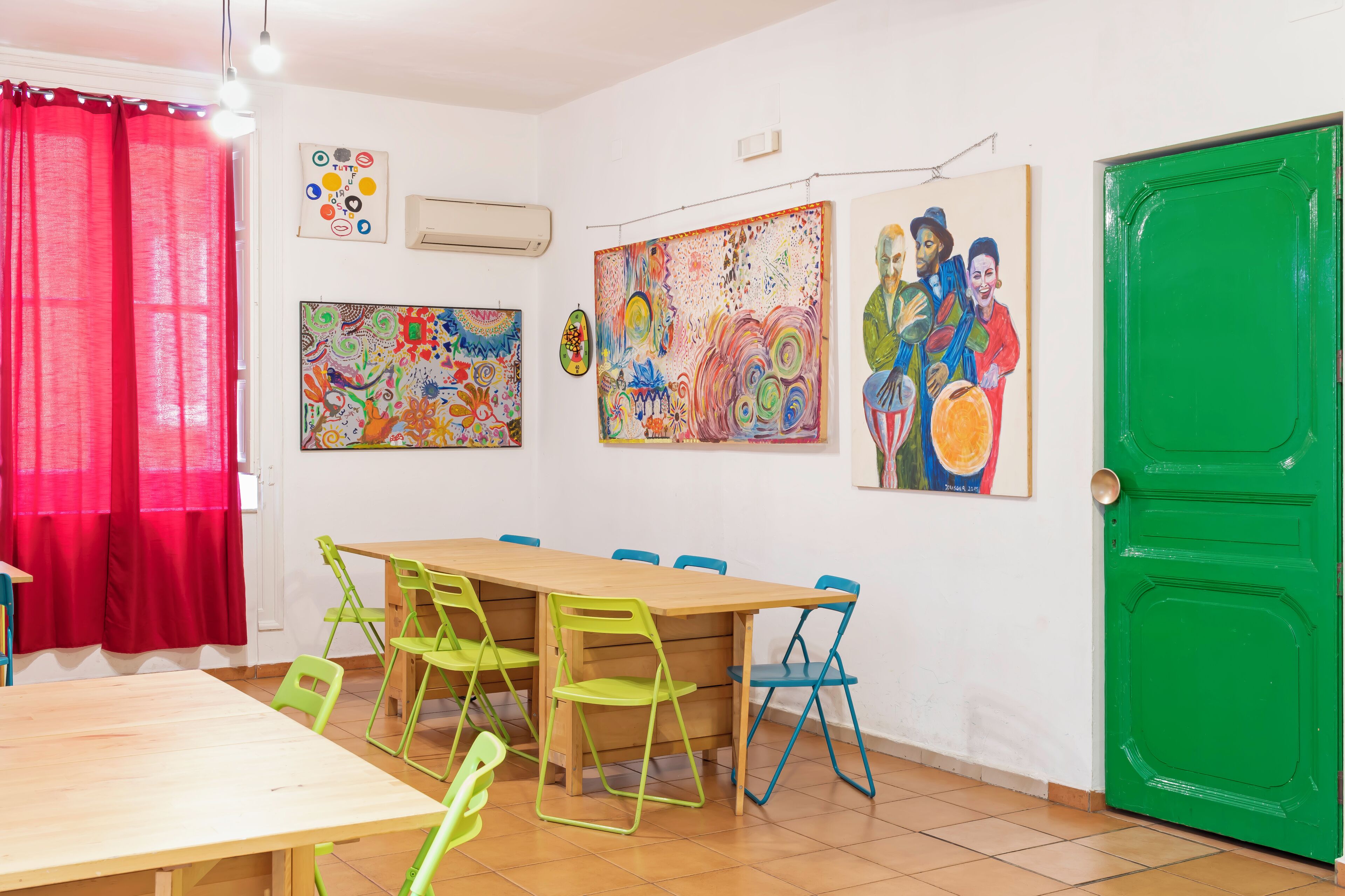 A room with a wooden table and chairs, a green door, and colorful abstract paintings on the walls.