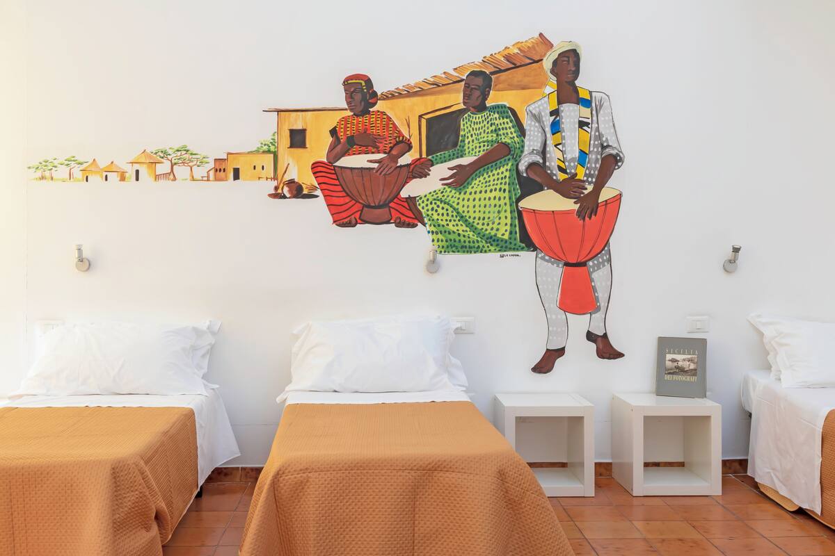 Ein Hotelzimmer mit zwei Betten, einem Wandgemälde, das eine traditionelle Szene zeigt, und einem kleinen Tisch mit einem Buch.