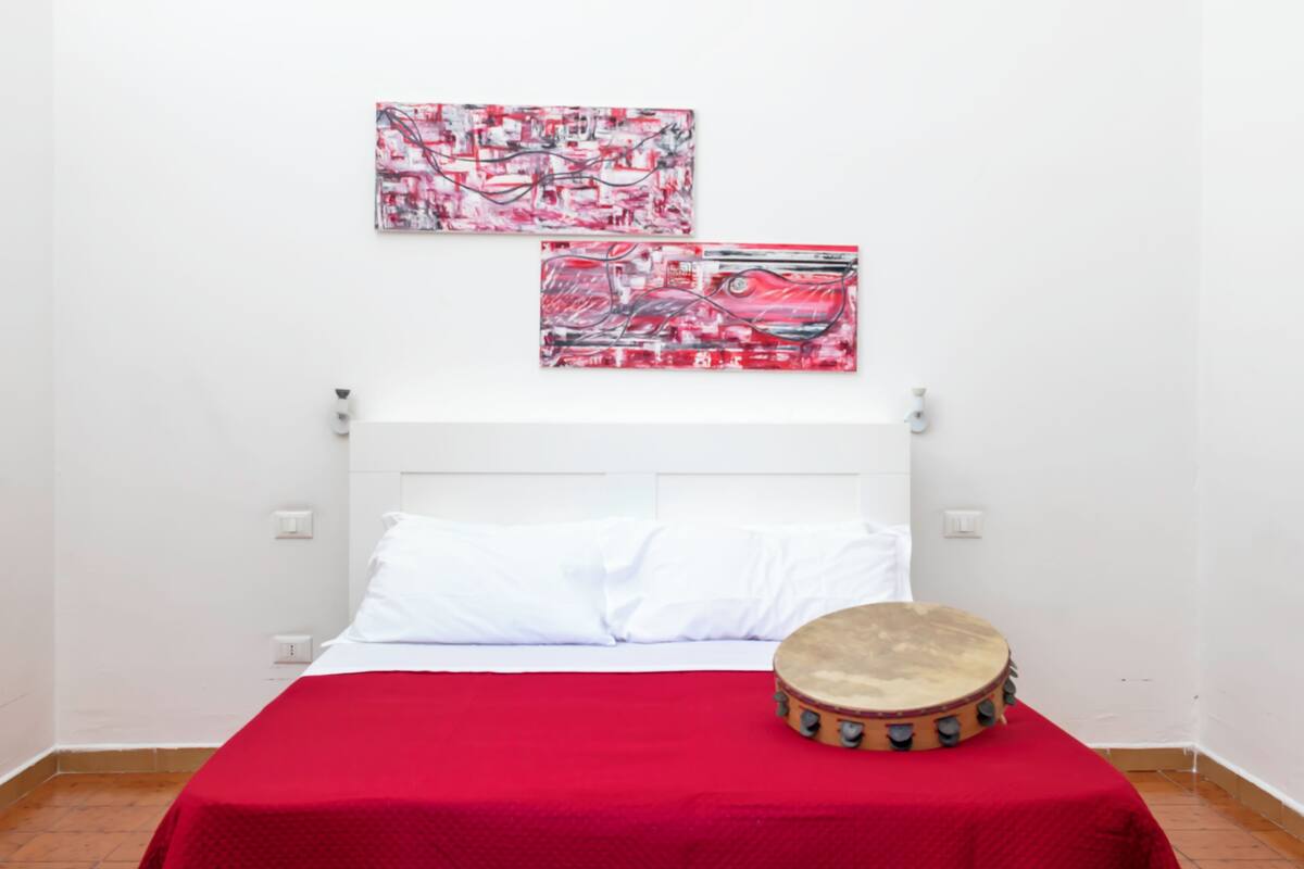 Ein Bett mit weißer Bettwäsche, einer roten Decke und einer Trommel auf dem Boden.