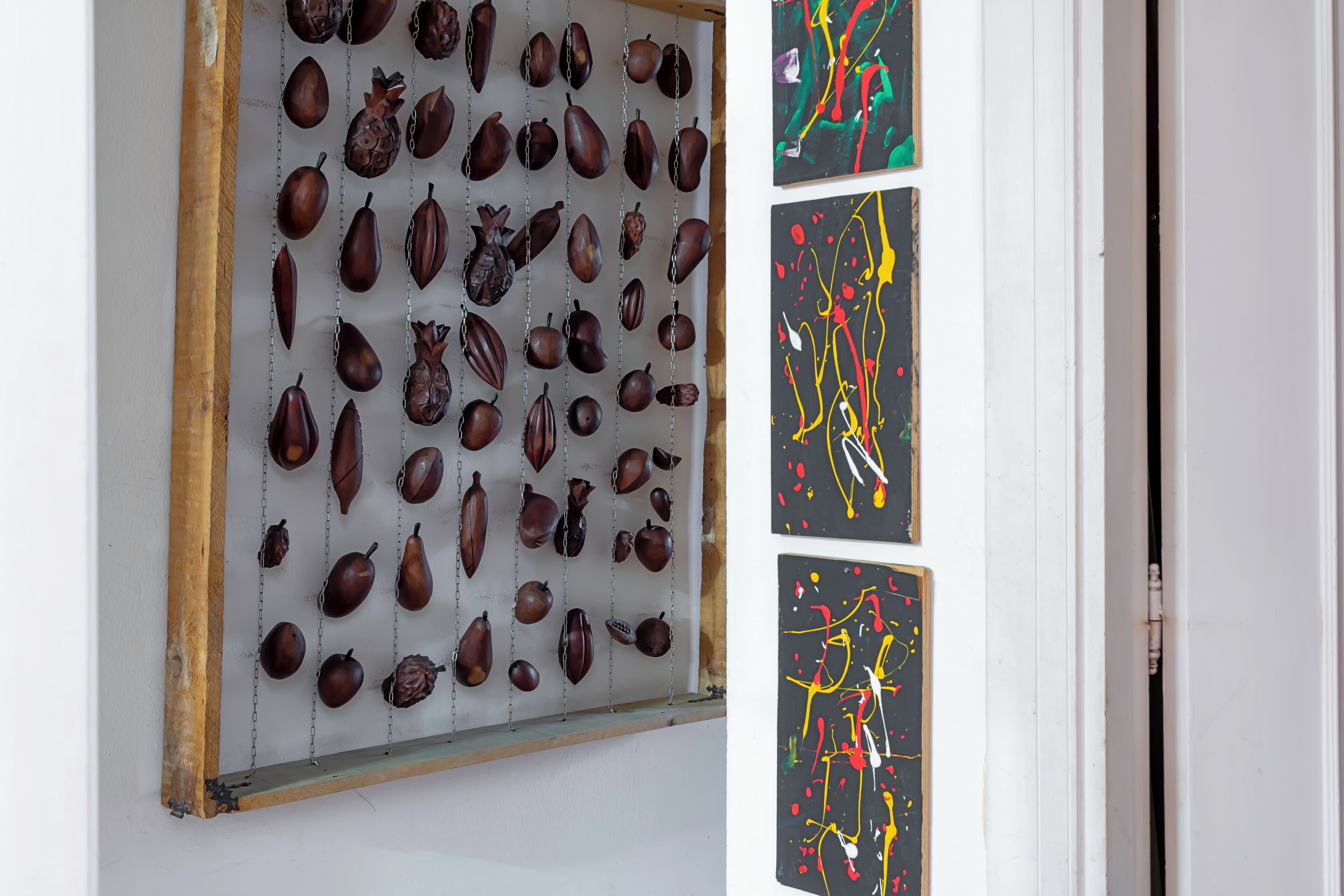 Una pared con una colección de frutas y verduras secas, y tres pinturas abstractas.