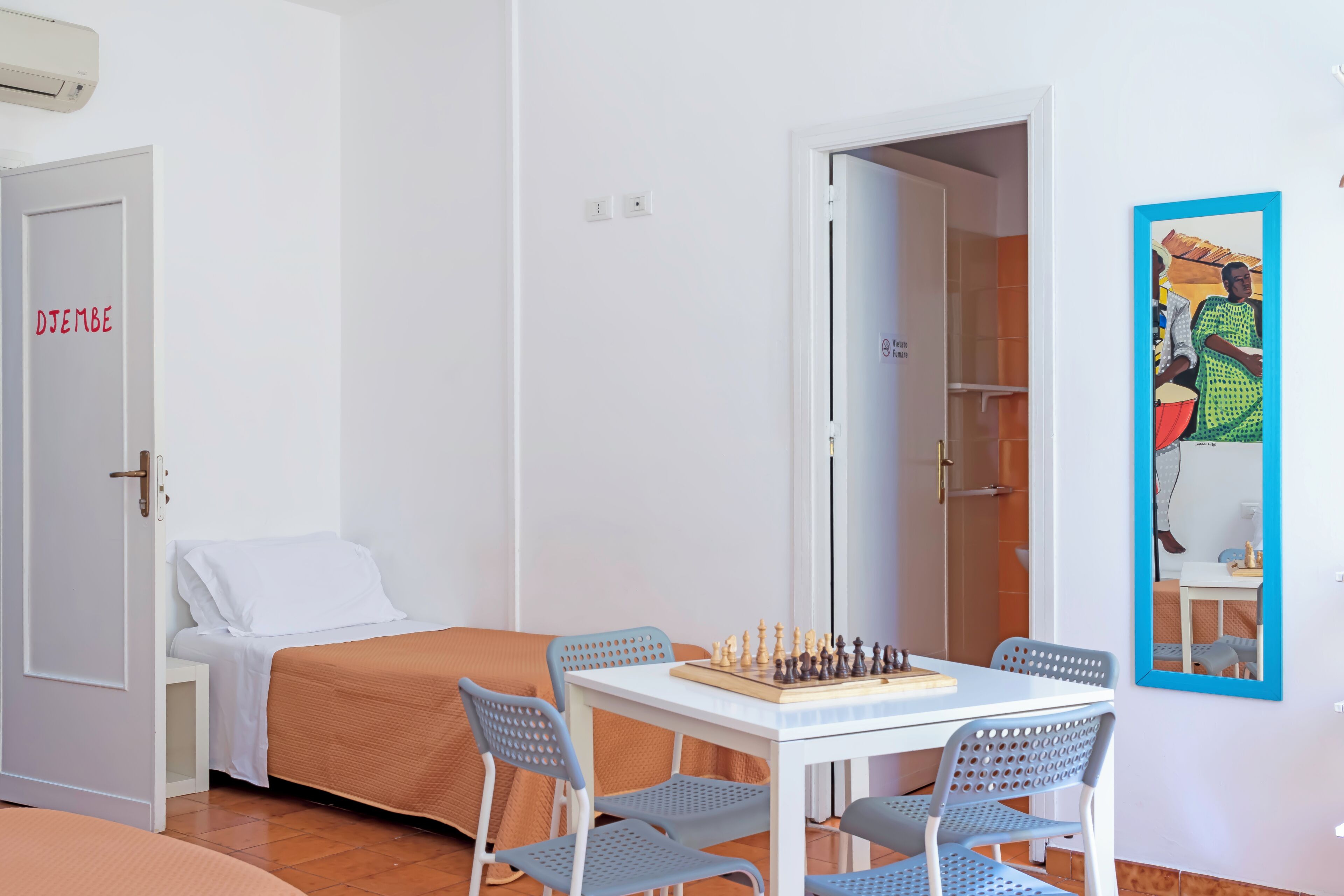 A room with a bed, a table with chess, and a door labeled "DJEMBE".