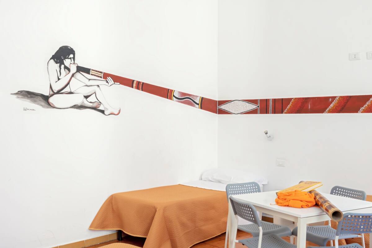 Ein Zimmer mit einem Bett, einem Tisch mit Stühlen und einer Wand mit Wandgemälde.