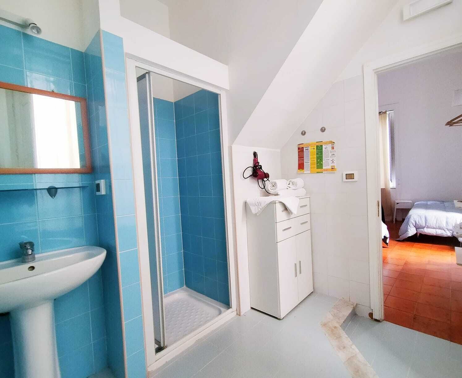 A bathroom with a sink, shower, and a white cabinet with towels.