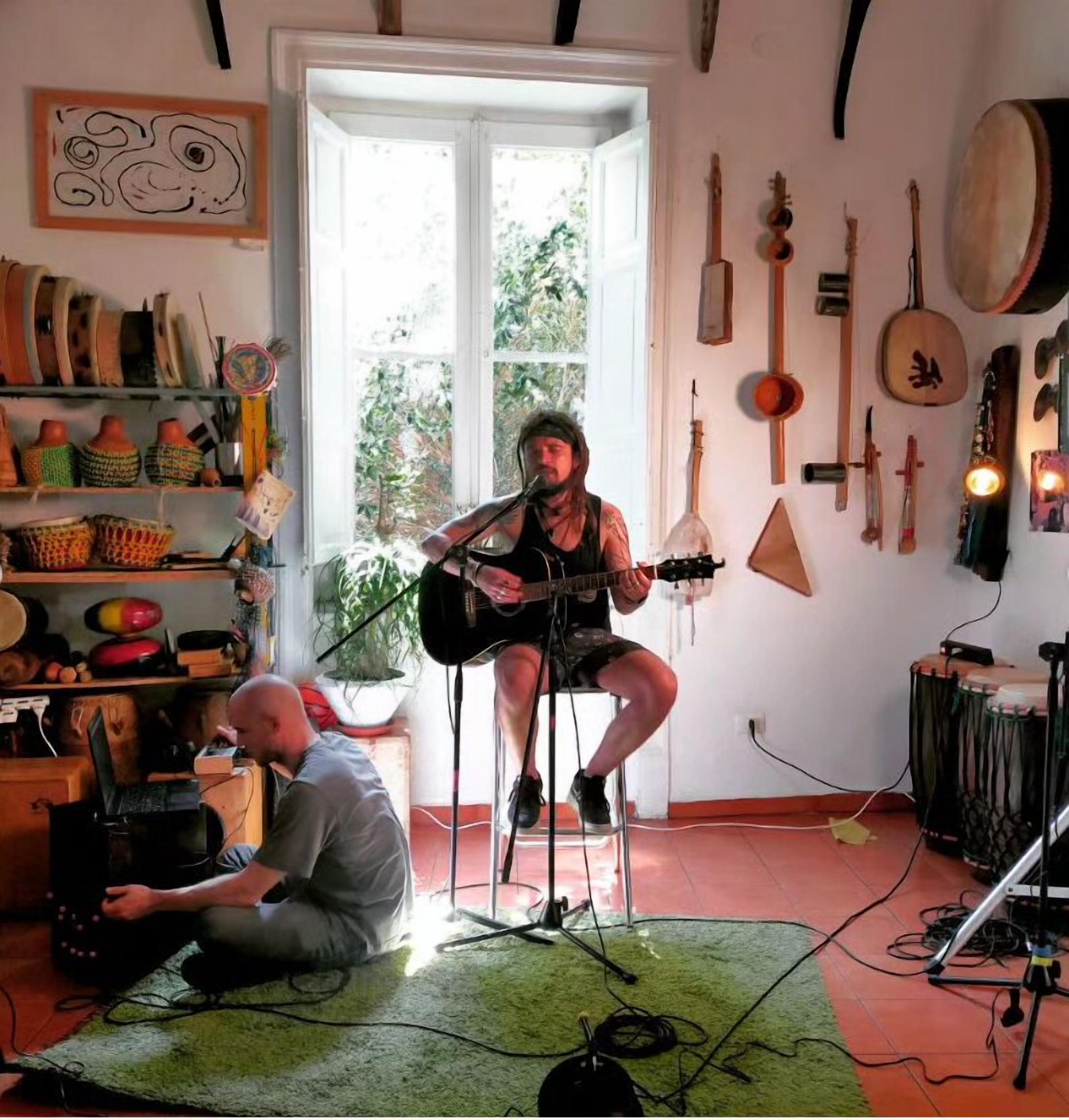 Ein Zimmer mit einem Gitarristen, einem Laptop auf dem Boden und verschiedenen Musikinstrumenten an den Wänden.