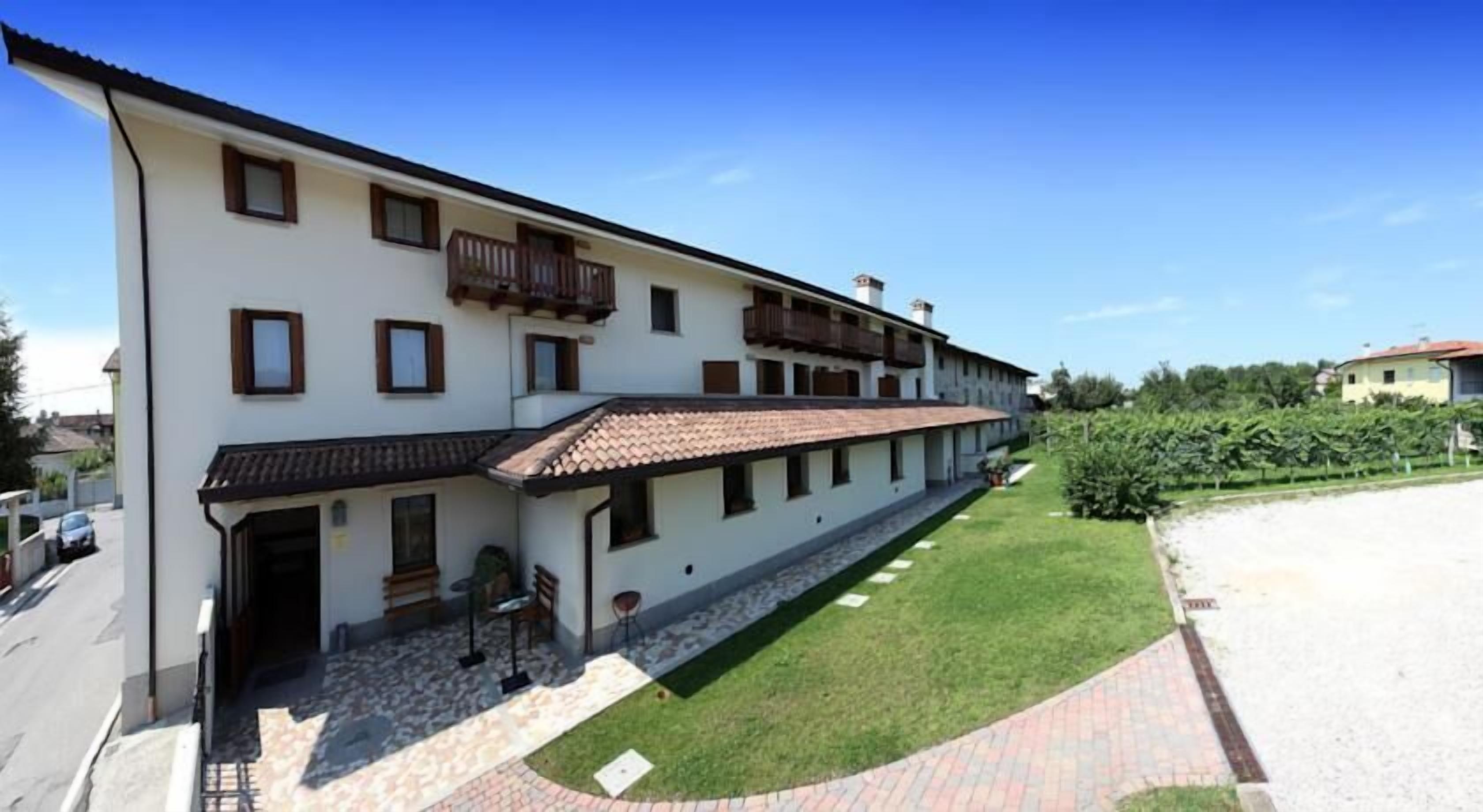 Un edificio a due piani con tetto in tegole, un piccolo giardino antistante e un vialetto lastricato.