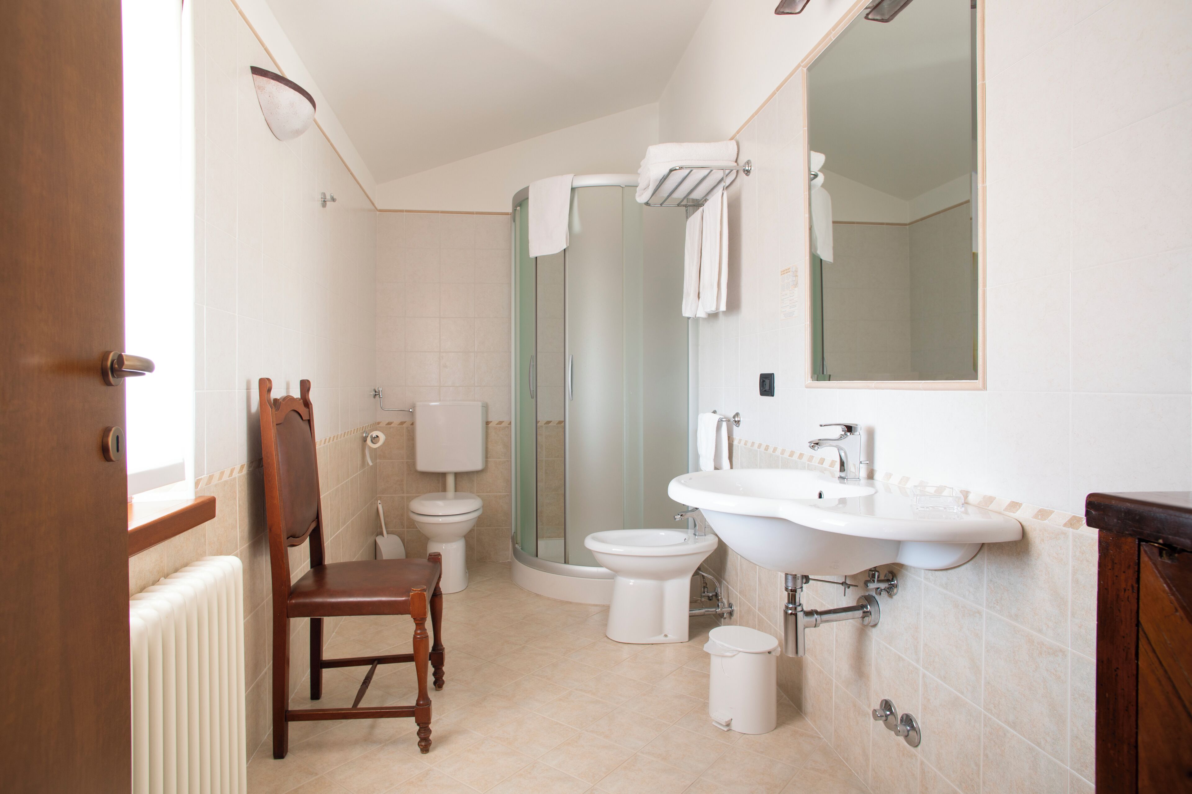 A bathroom with a wooden chair, a glass shower enclosure, a white sink, and a toilet.