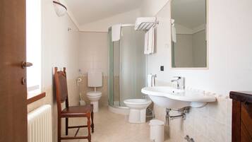 Une salle de bain avec une chaise en bois, une cabine de douche en verre, un lavabo blanc et des toilettes.