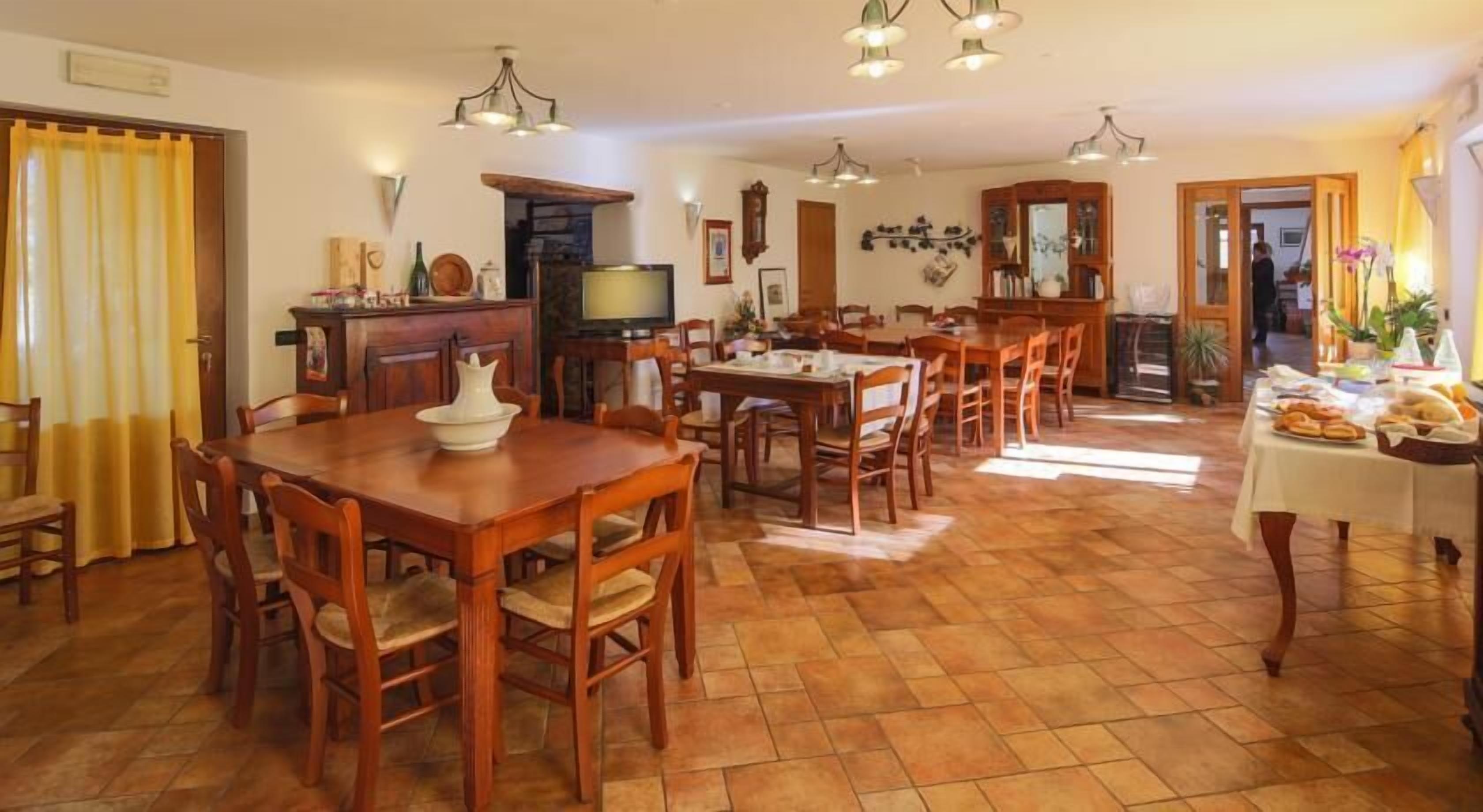 A spacious dining area with wooden tables and chairs, a television, and a kitchen area in the background.